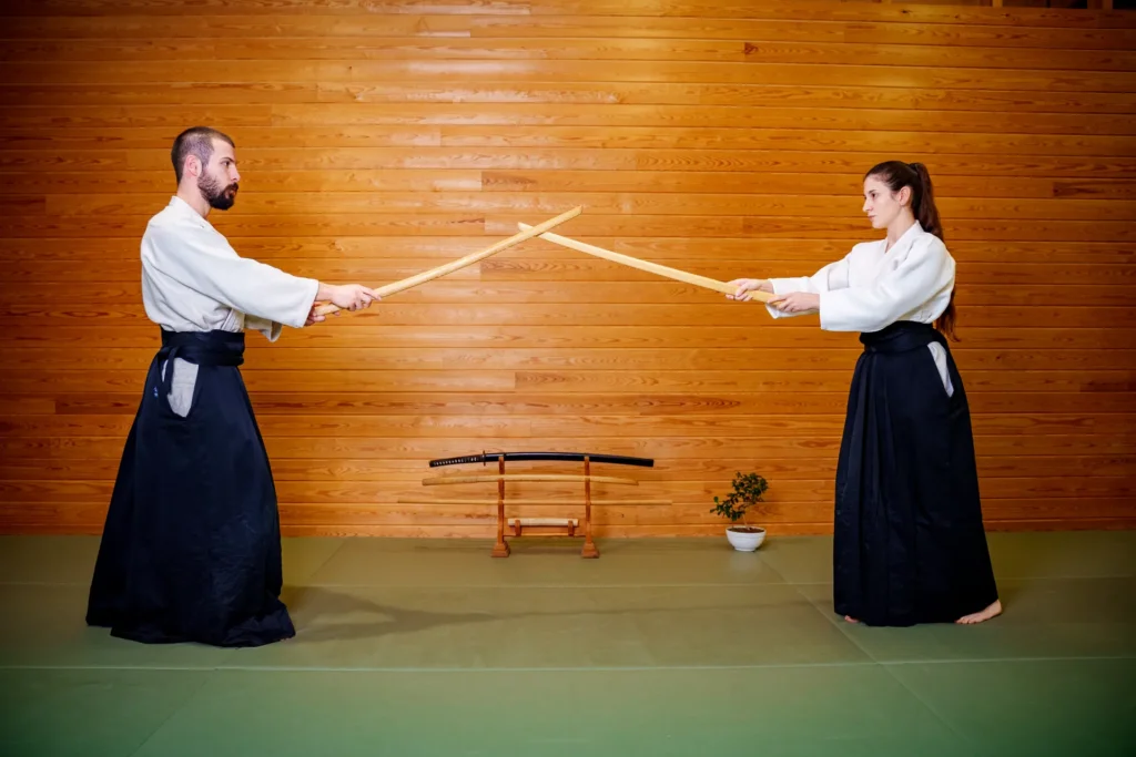 İki aikidoka ahşap duvar önünde bokken ile karşılıklı çalışıyor (kumitachi), Katsu Ankara, Çayyolu.