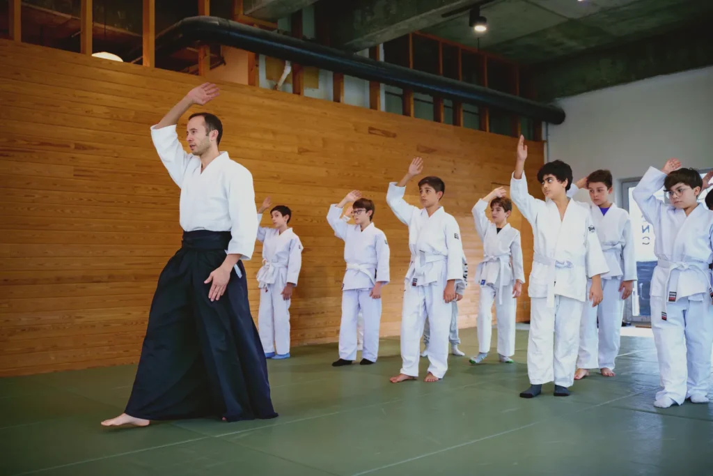 Hakamalı eğitmen kolunu kaldırıyor, çocuk aikido grubu sıra hâlinde hareketi tekrar ediyor, Katsu Ankara, Çayyolu.